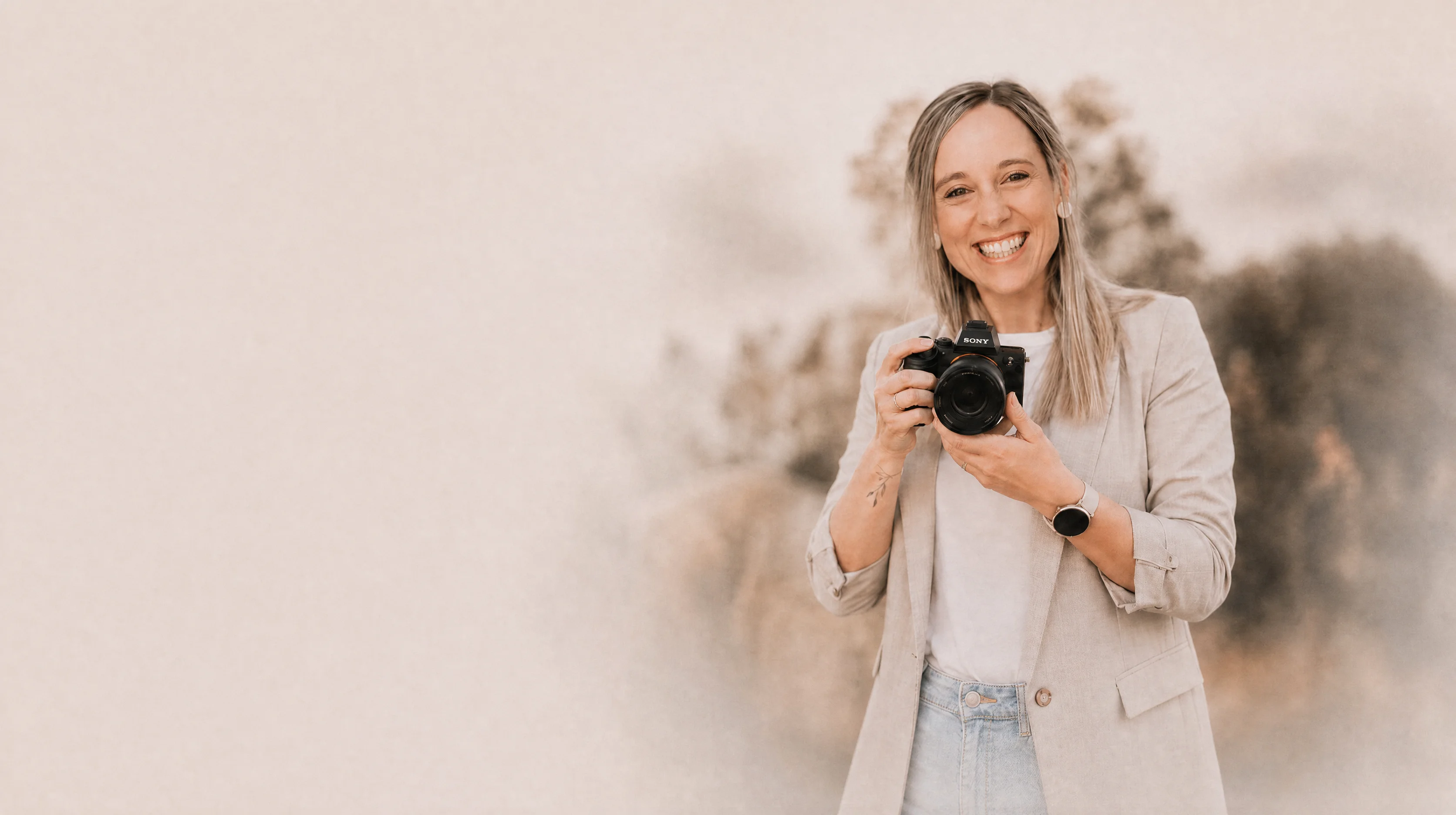 Fotografin Nicole Schwaiger mit Kamera vor weichem Naturhintergrund